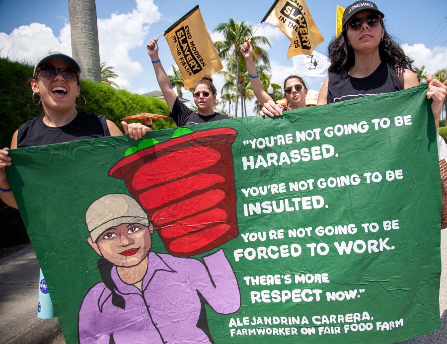 Women in sunglasses holding a green banner protesting. The green banner reads "You're not going to be Harassed. You're not going to be insulted. you're not going to be forced to work. There's more respect now." Alejandrina caraera. Farmworker on Fair food farm